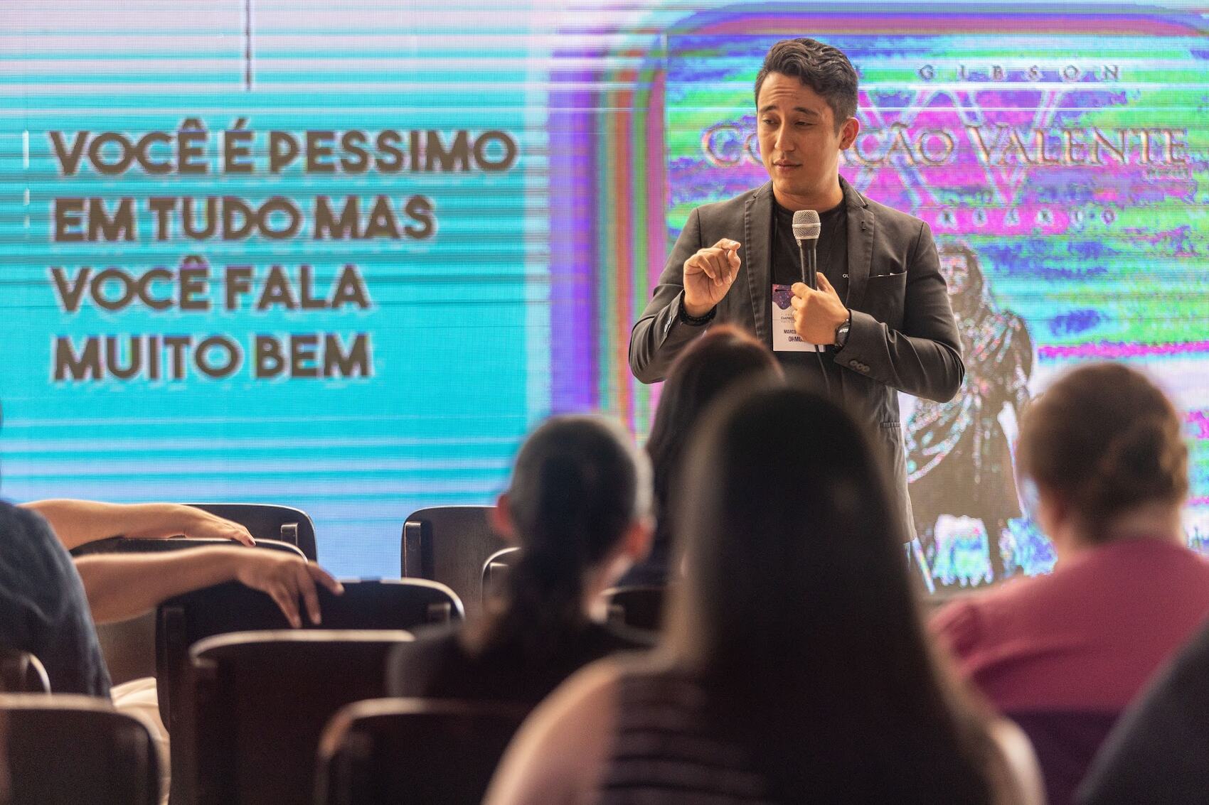 Marco no palco; no telão, a frase: você é péssimo em tudo mas você fala muito bem